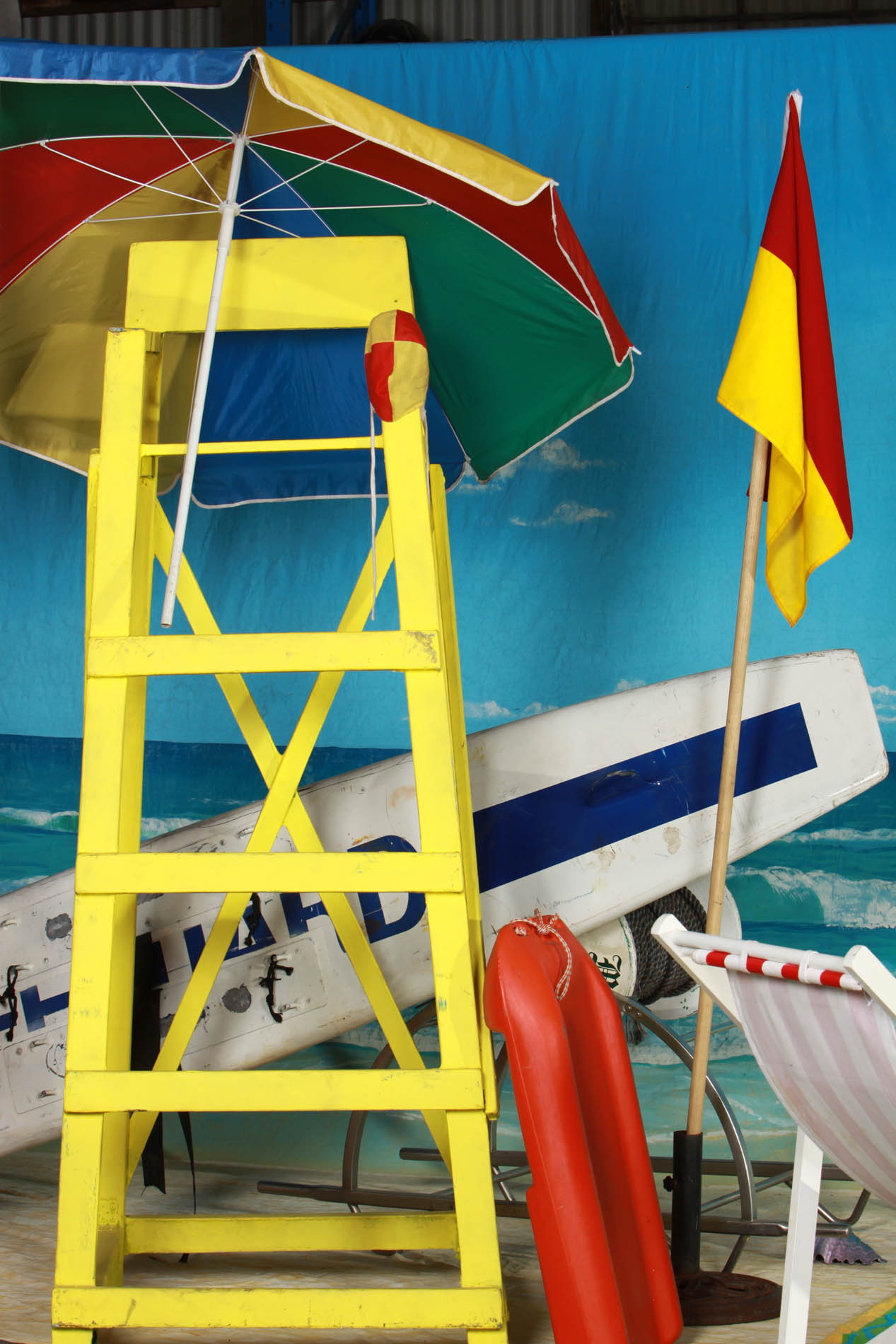 Yellow lifeguard tower beside a rainbow beach umbrella, red and yellow patrol flag, rescue board and rescue tube