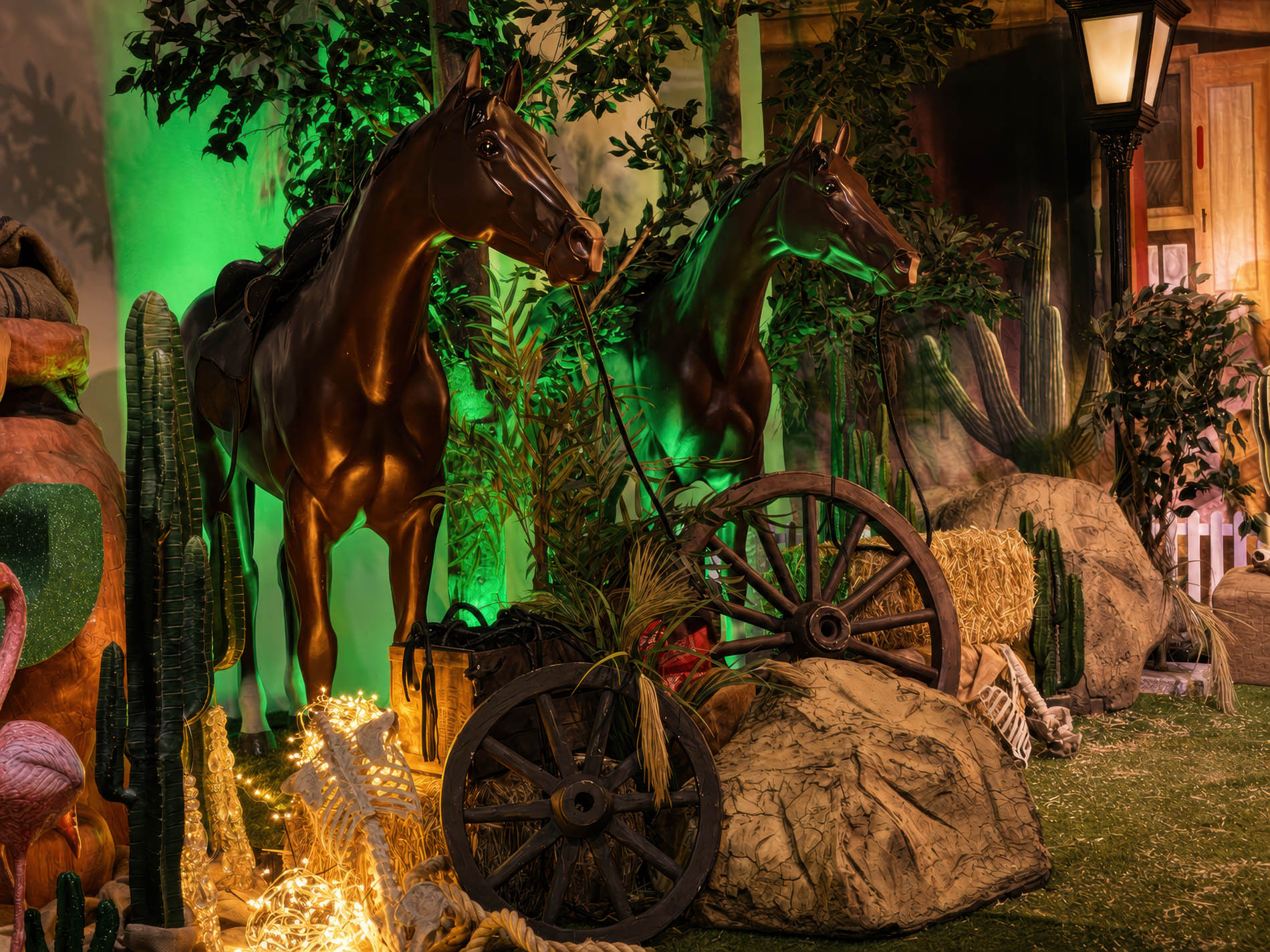 Two bronze horse figures beside a wagon wheel, hay bale, and saguaro cacti